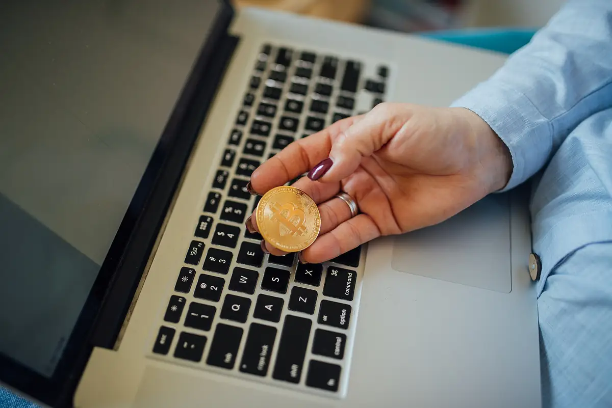 A hand holds a gold coin over a laptop keyboard.